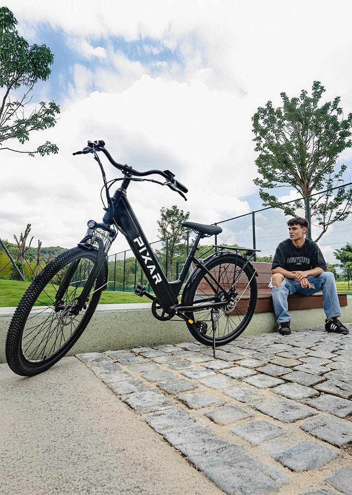 Person sitting on a bench next to a black electric bike with 'PYXAR' branding in an outdoor setting.