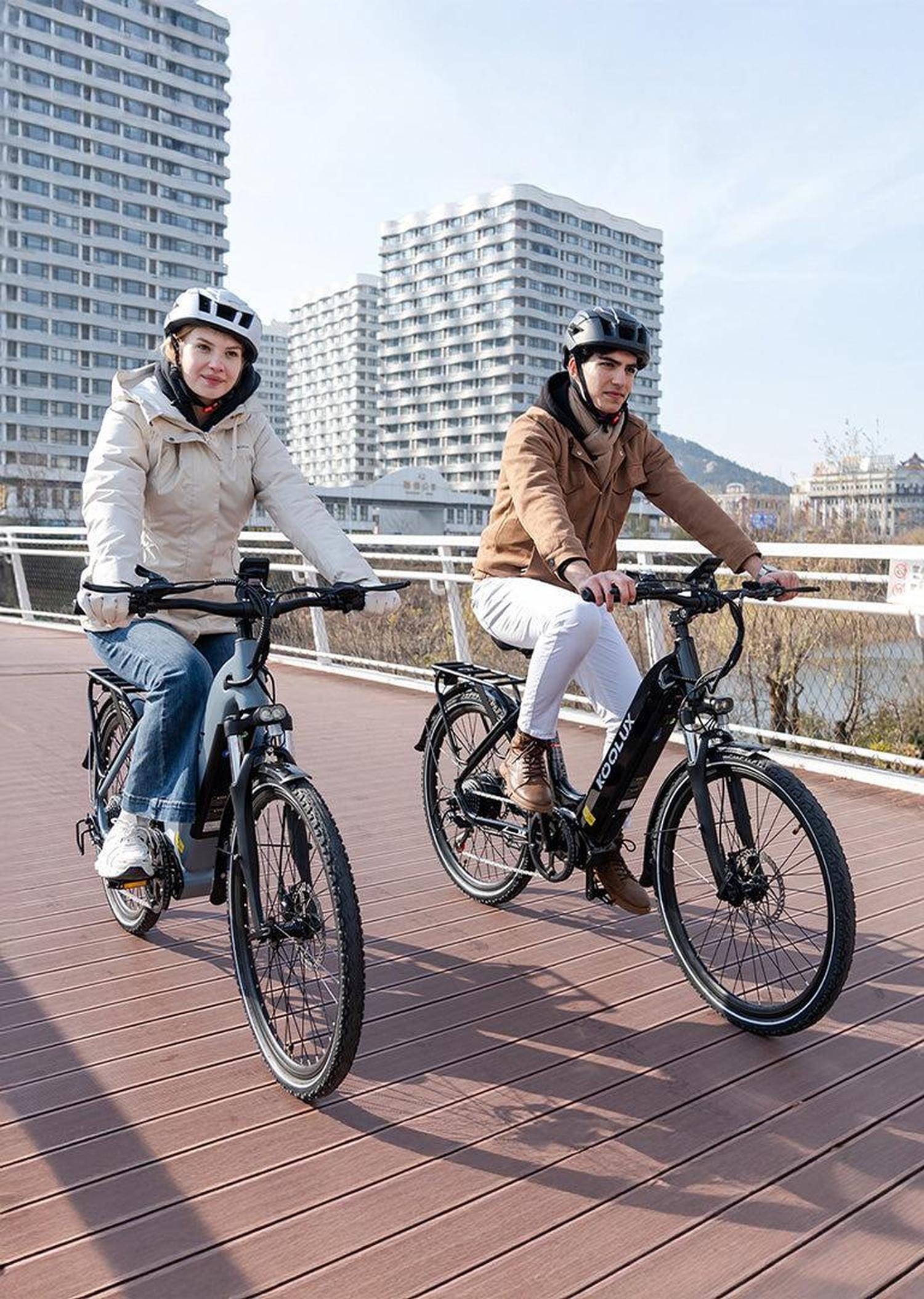 Two people riding electric bikes on a bridge with buildings in the background