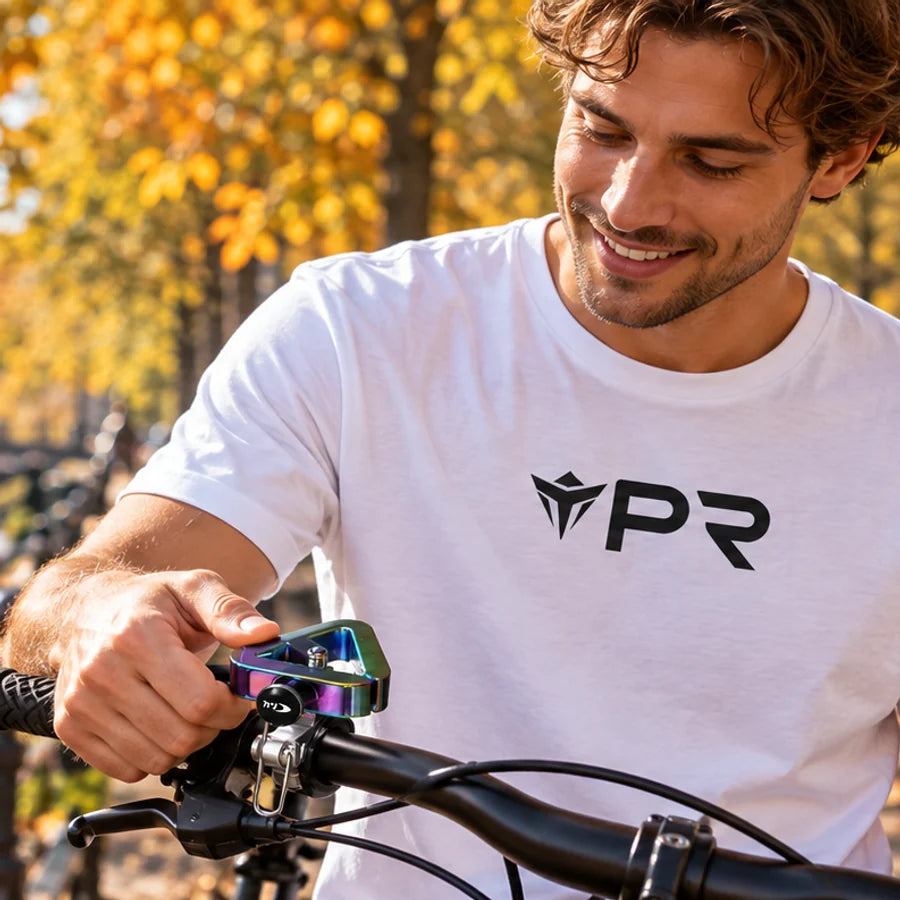 Rider in a white Punk Ride T-shirt using an iridescent bicycle bell beside an autumn canal.