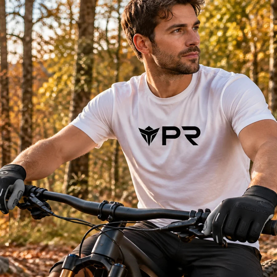 A person in a white Punk Ride logo T-shirt wearing the exact black Endura full-finger gloves, clearly visible while gripping the handlebars of a parked bicycle in an autumn setting. Mobile collection banner.