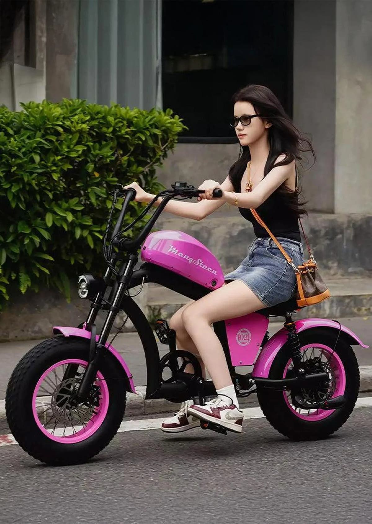 Woman riding a pink and black electric bike on a street.