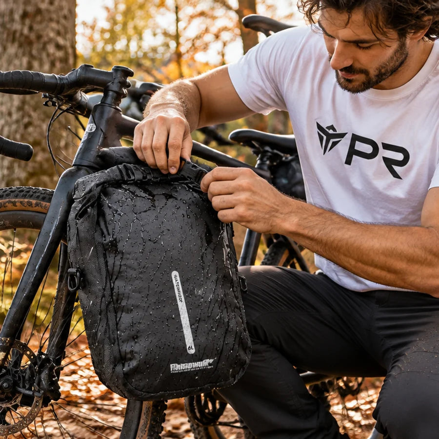 A person in a white Punk Ride logo T-shirt closing the roll top of the exact black 6 L Rhinowalk fork bag, attached low on a parked bicycle fork in an autumn setting. Mobile collection banner.