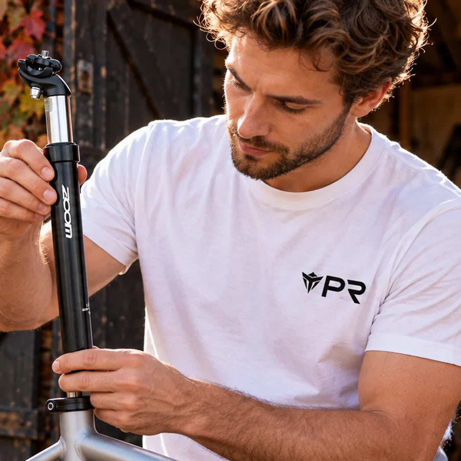Rider in a white Punk Ride T-shirt fitting a black and silver ZOOM suspension seatpost at an autumn cycle workshop.