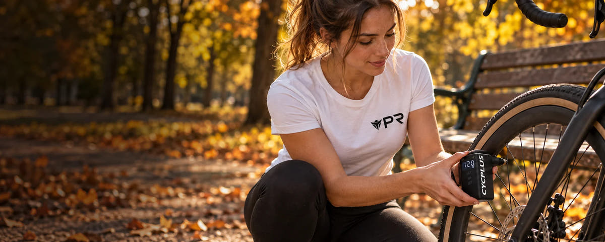 Woman in a white Punk Ride T-shirt using a black CYCPLUS electric pump at a bicycle tyre valve in an autumn park.