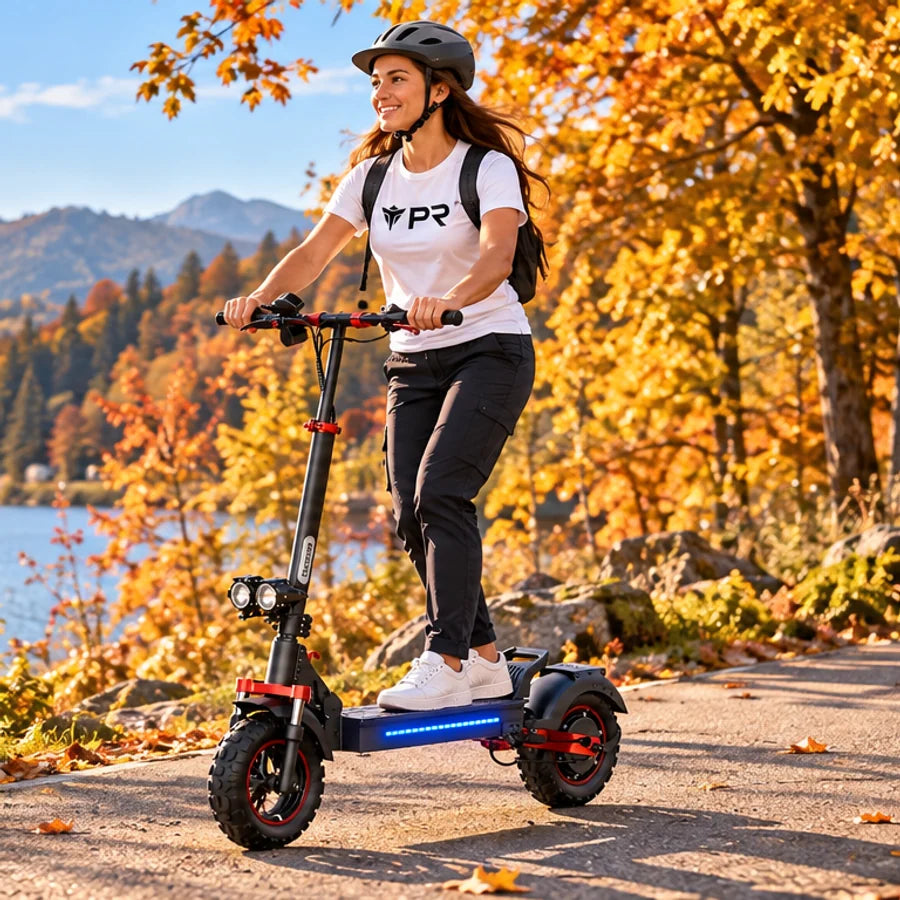 A helmeted rider wearing a white Punk Ride logo T-shirt rides a black and red ISCOOTER iX5S with wide knobbly tyres beside an autumn lake. Mobile collection banner.