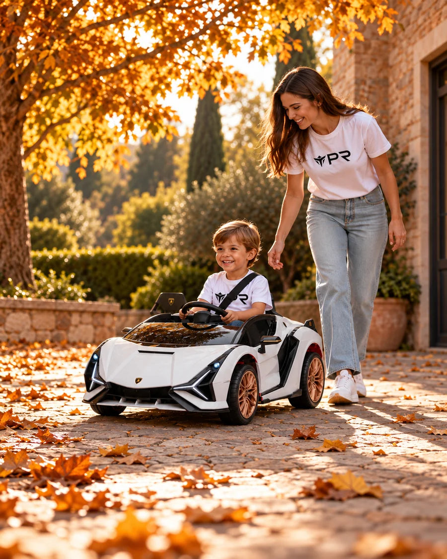 A child drives a white Lamborghini Sian ride-on toy beside an adult in white Punk Ride logo T-shirts in an autumn courtyard.
